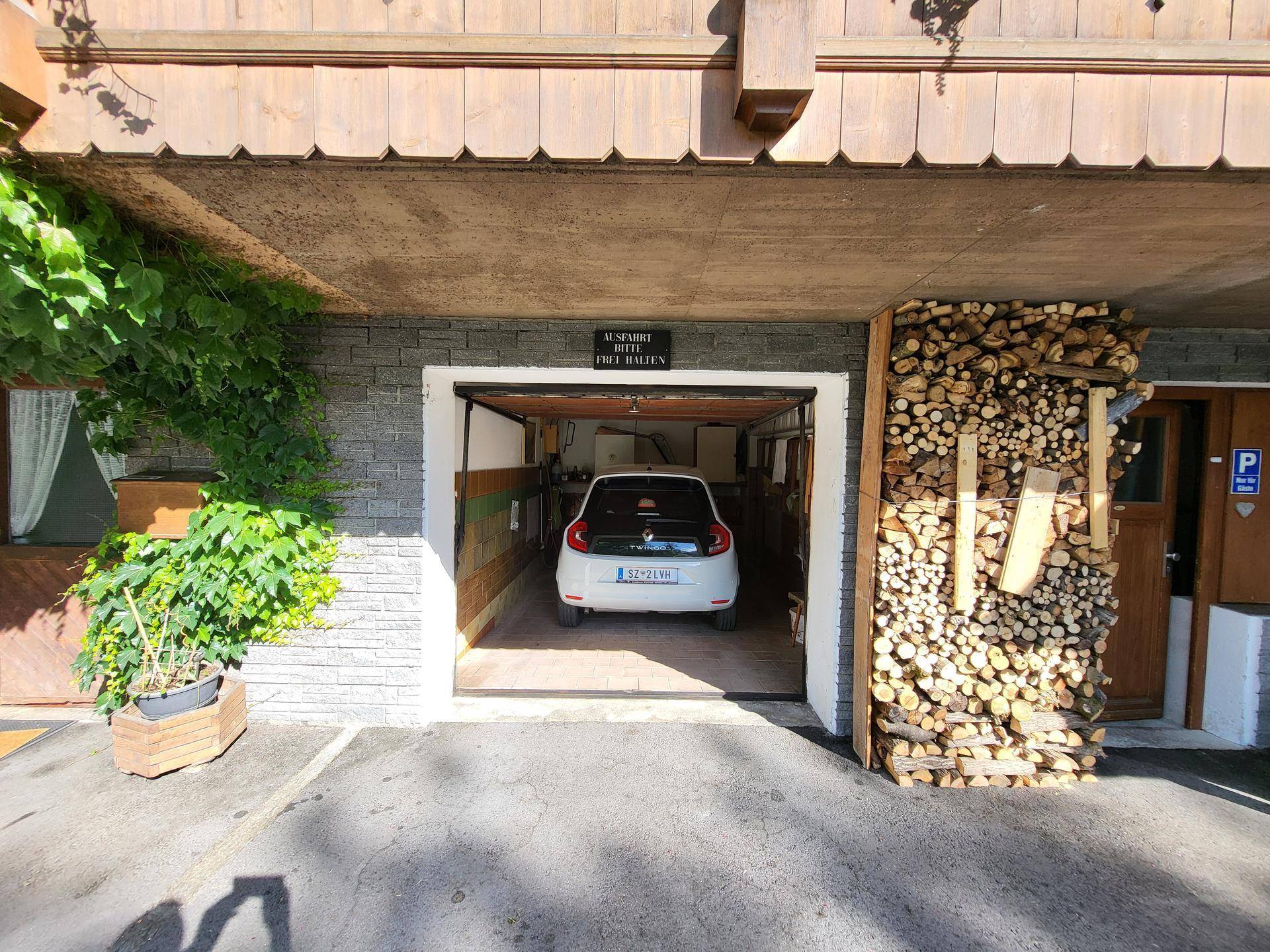 Einzelgarage mit geparktem Auto und gestapeltem Brennholz daneben.