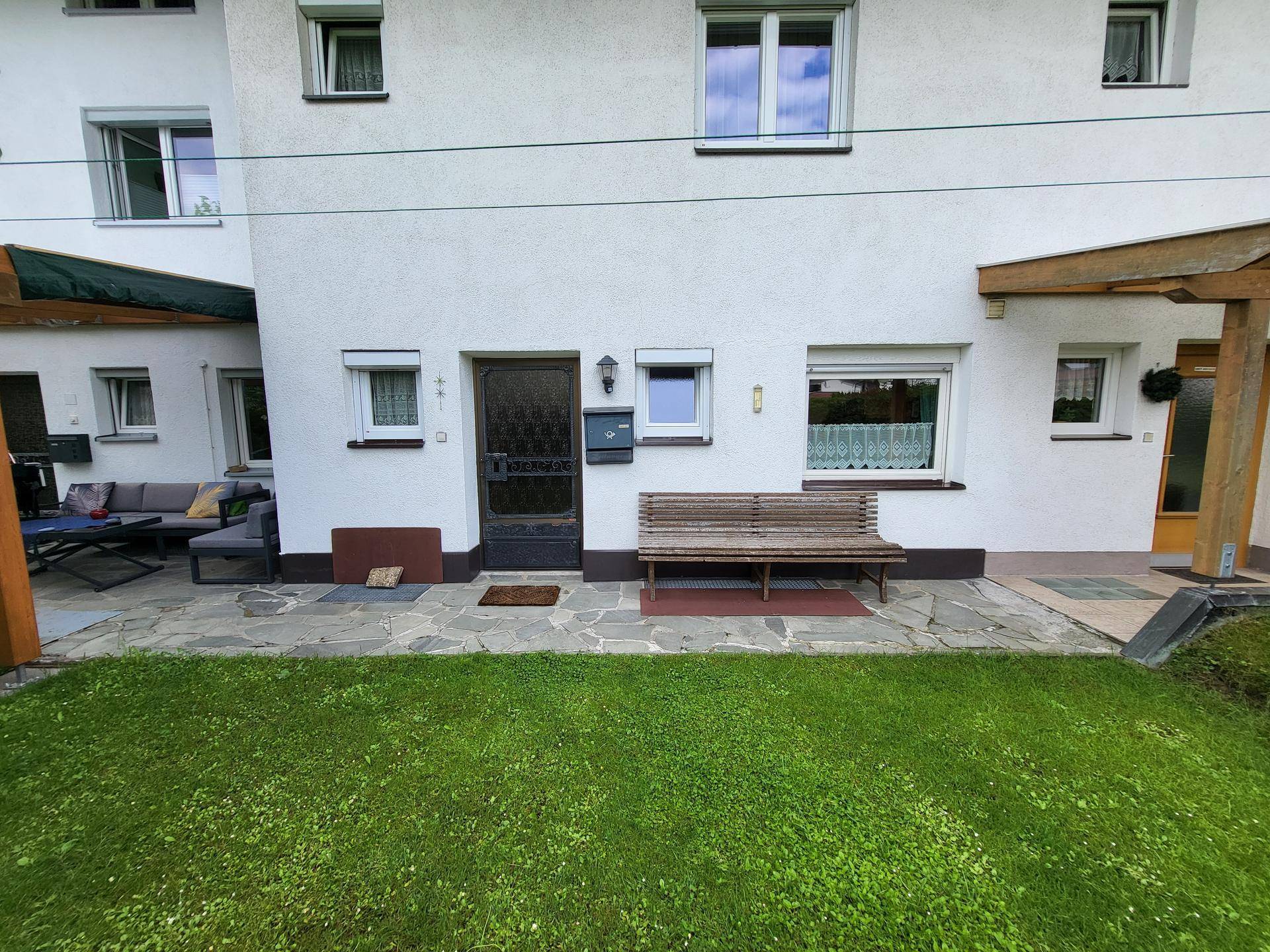 Gemütlicher Gartenbereich mit Steinterrasse, Holzbank und Rasenfläche vor dem Haus.