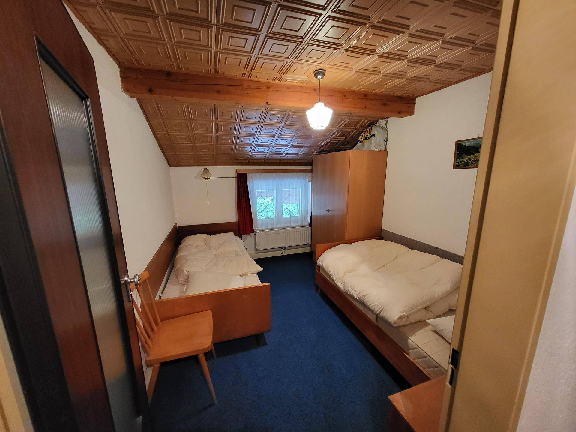 Schlafzimmer mit zwei Einzelbetten, blauem Teppichboden und Holzdecke mit sichtbaren Balken.