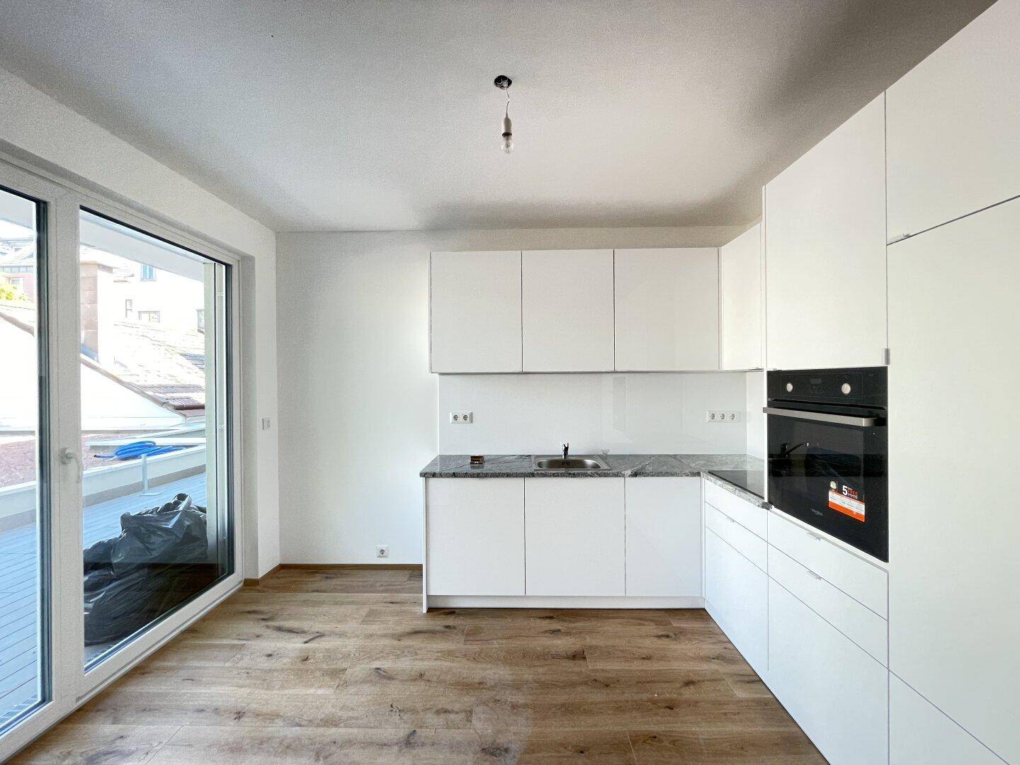 Moderne weiße Küche mit Granitarbeitsplatte, integriertem Backofen und Zugang zur Terrasse.