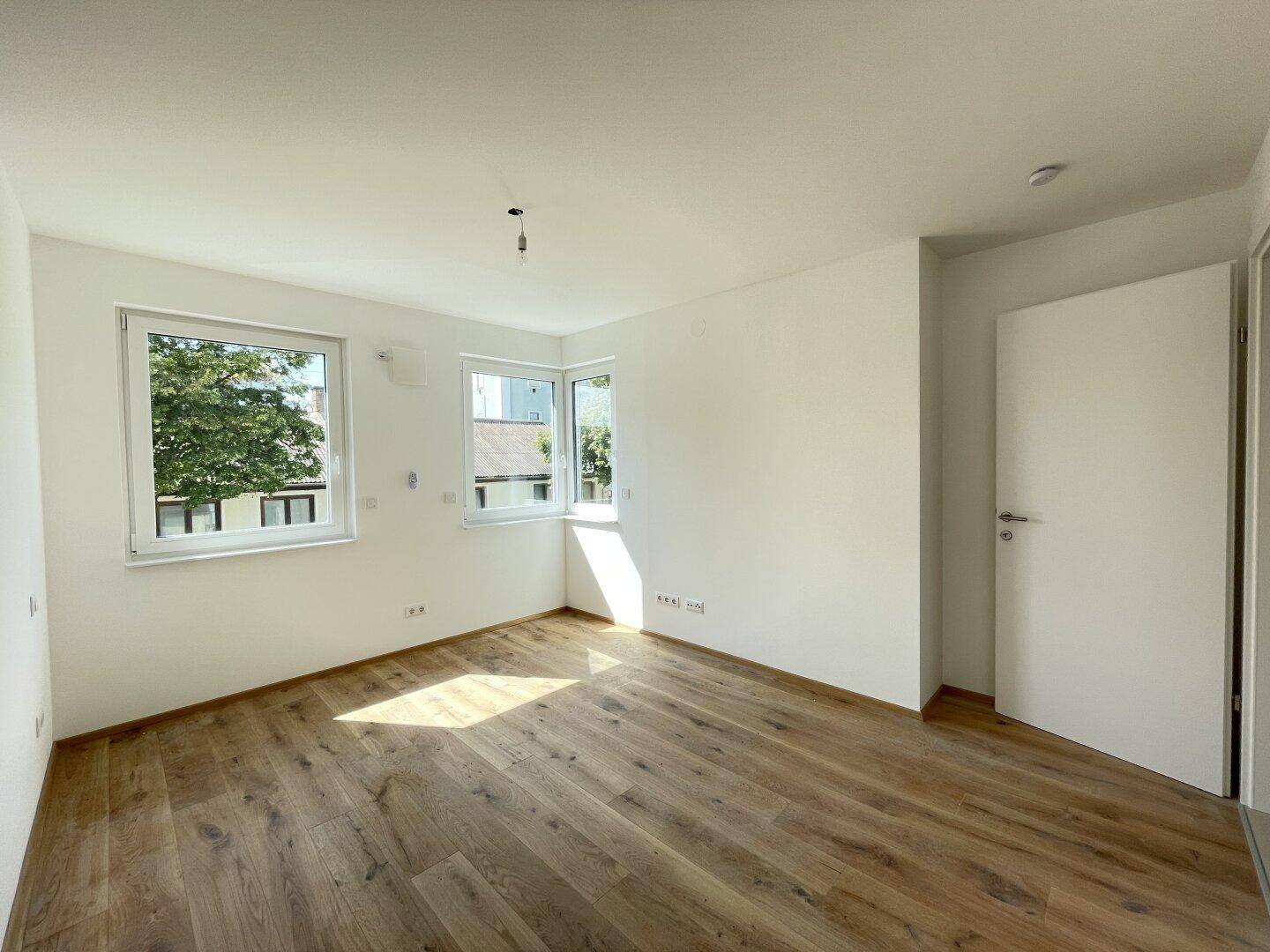 Helles Schlafzimmer mit neuem Parkettboden, weißen Wänden und Blick ins Grüne.