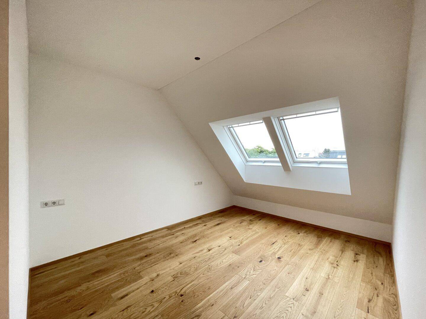 Helles Zimmer mit Holzboden, Dachschrägen und zwei Dachfenstern für viel Tageslicht.