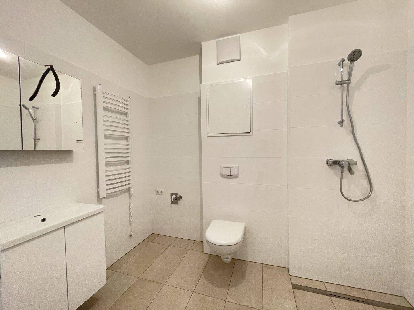 Modernes Badezimmer mit weißen Fliesen, Dusche, WC und beheiztem Handtuchhalter.