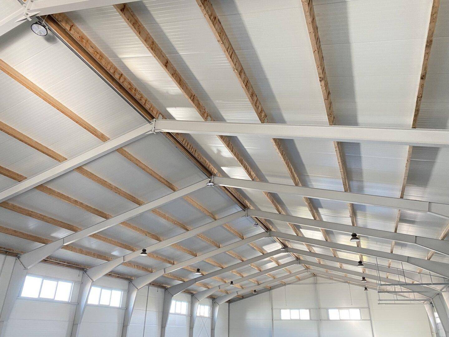 Blick zur Decke einer Lagerhalle mit sichtbaren Holz- und Metallträgern sowie Oberlichtern.