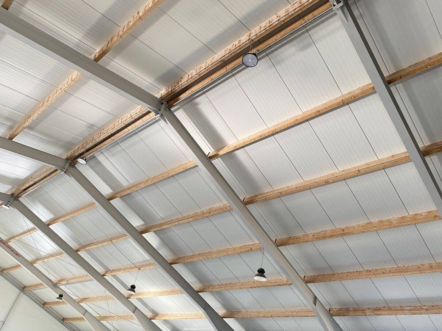 Deckenkonstruktion einer Industriehalle mit Holzbalken, Metallstreben und Beleuchtungselementen.