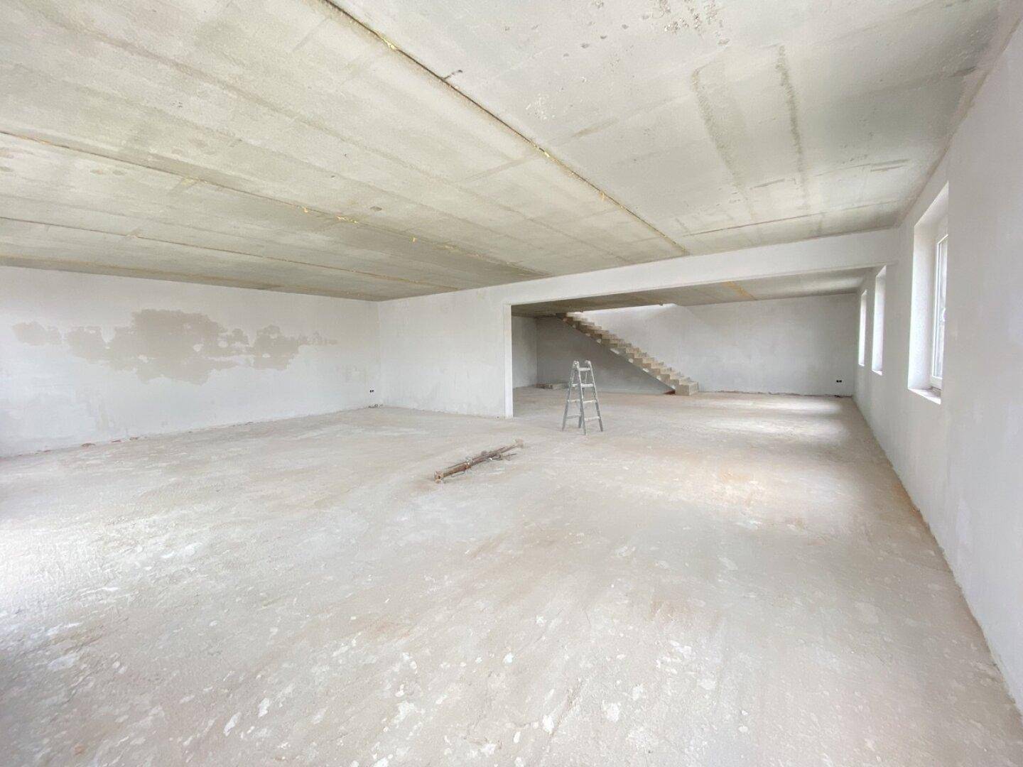 Großer, leerer Raum im Rohbau mit Betondecke und Wänden, bereit für den weiteren Ausbau.