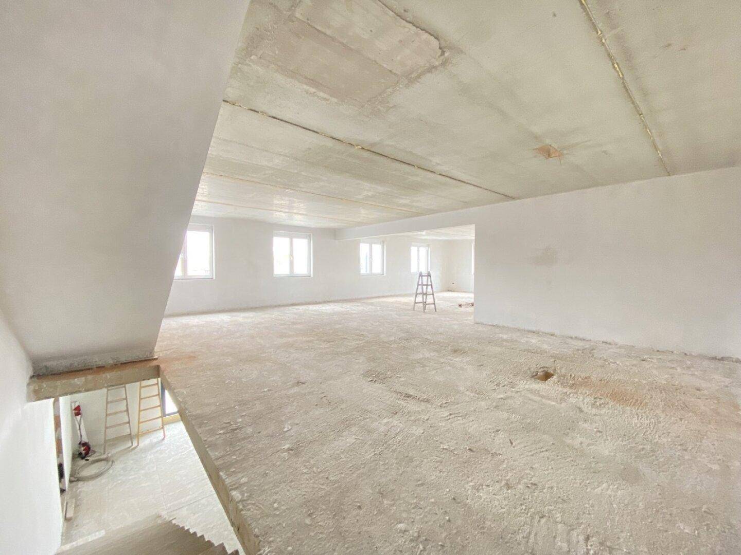 Weitläufiger Rohbau eines Bürobereichs mit Betondecke und Blick auf eine Treppe, viel Potenzial.