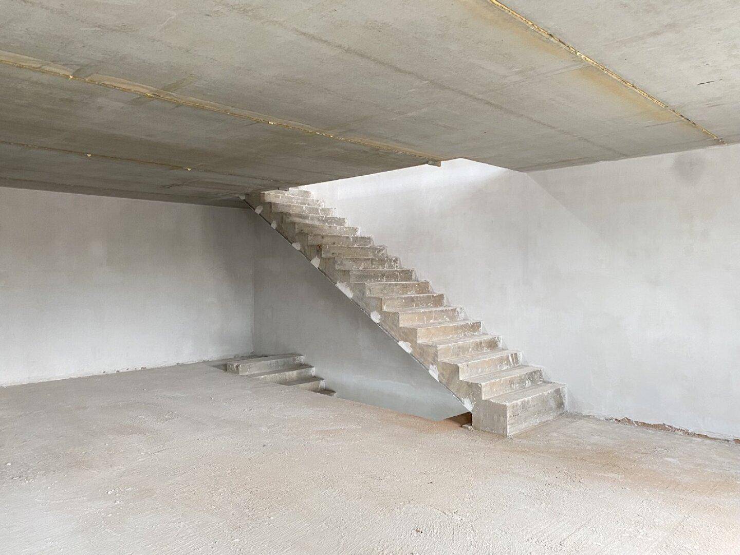 Treppe im Rohbau eines Bürogebäudes mit Betondecke und unverputzten Wänden, funktionaler Stil.