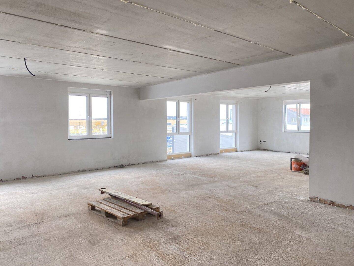 Heller Rohbau eines Bürobereichs mit großen Fenstern und einer Palette, bereit für den Innenausbau.