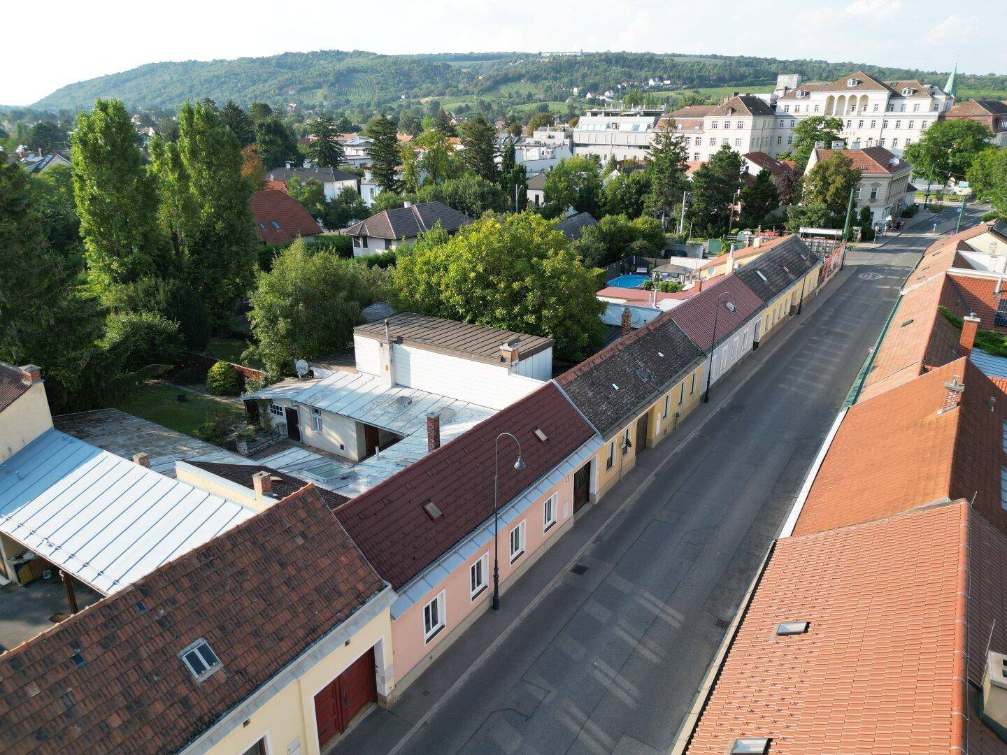 Luftaufnahme einer Straße mit Reihenhäusern und einem bewaldeten Hügel im Hintergrund.