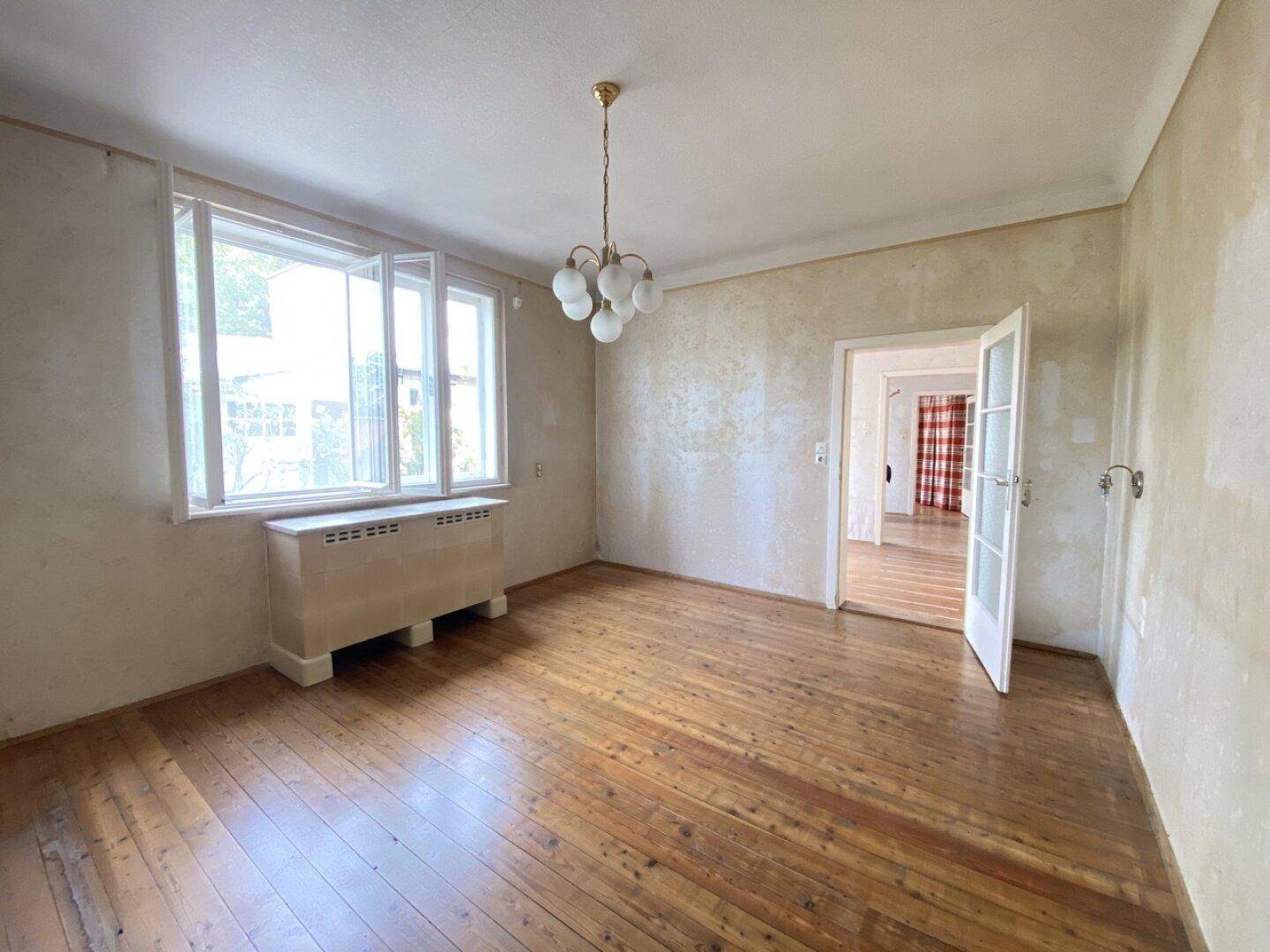 Geräumiges Zimmer mit Holzdielenboden, hellen Wänden und einem großen Fenster.