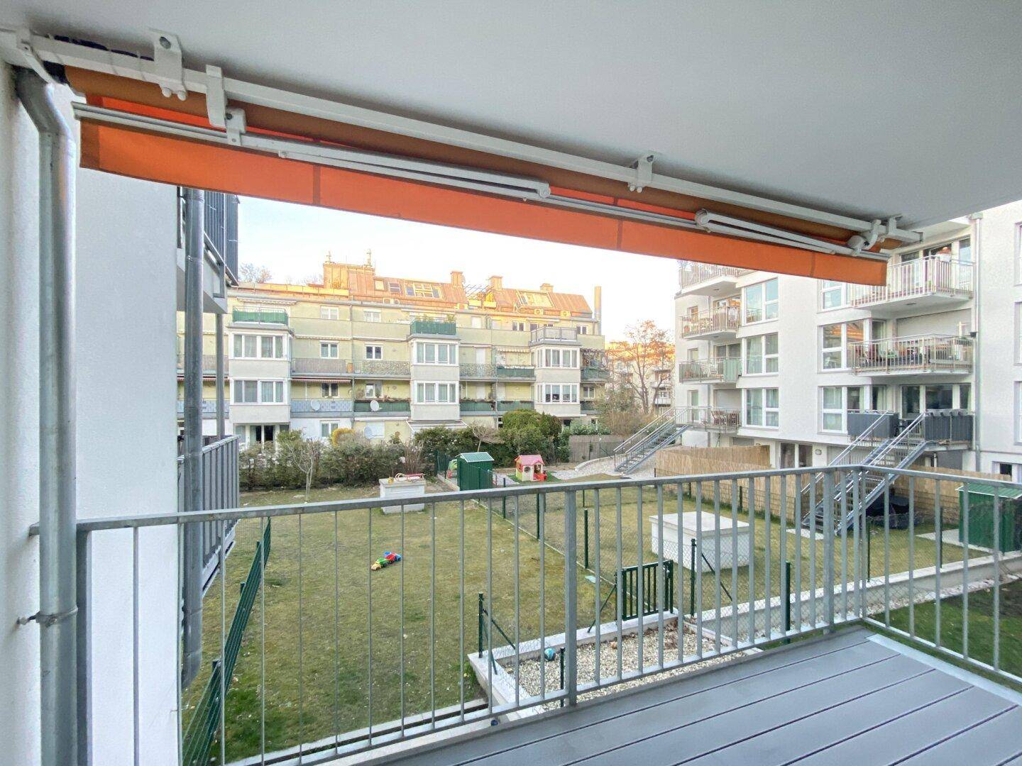 Balkon mit Markise und Blick auf den begrünten Innenhof mit Spielplatz.