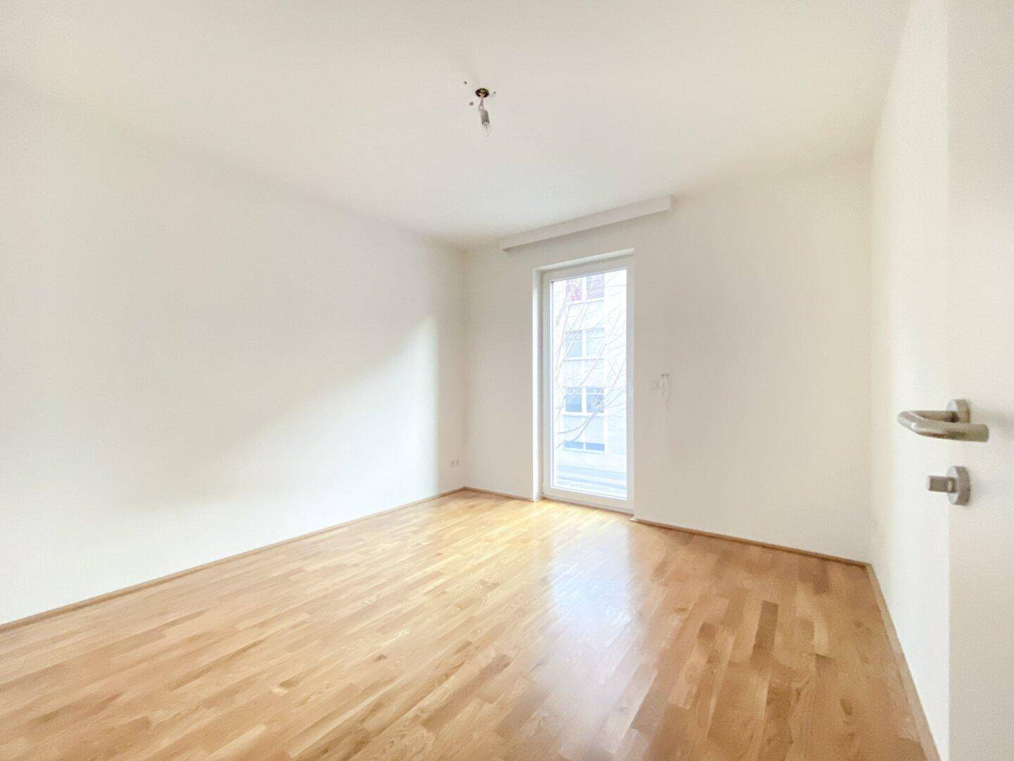 Geräumiges Schlafzimmer mit hellem Parkettboden und viel Tageslicht durch die große Fenstertür.