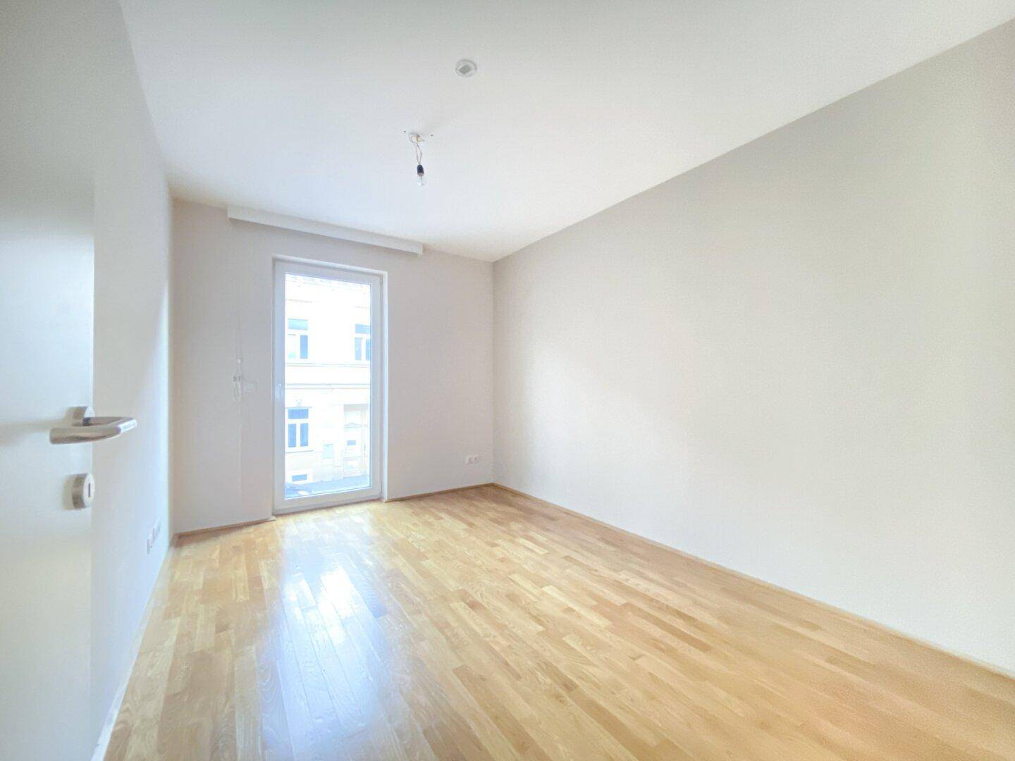 Helles Schlafzimmer mit Parkettboden und Zugang zu einem Balkon oder einer Terrasse.