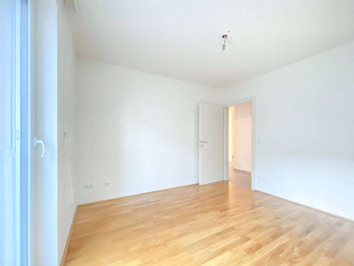 Lichtdurchflutetes Schlafzimmer mit Parkettboden und Zugang zum Flur, bereit zur individuellen Gestaltung.