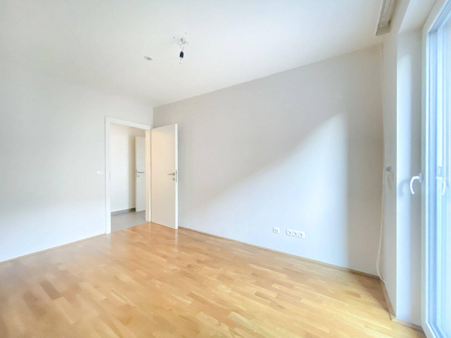 Helles Schlafzimmer mit Parkettboden und großen Fenstern, die eine angenehme Wohnatmosphäre schaffen.