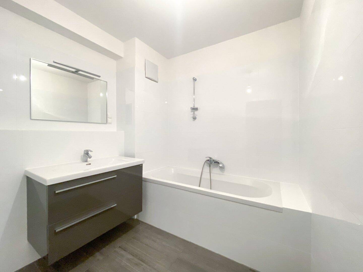 Modernes Badezimmer mit Badewanne, Waschtischunterschrank und großen weißen Wandfliesen.