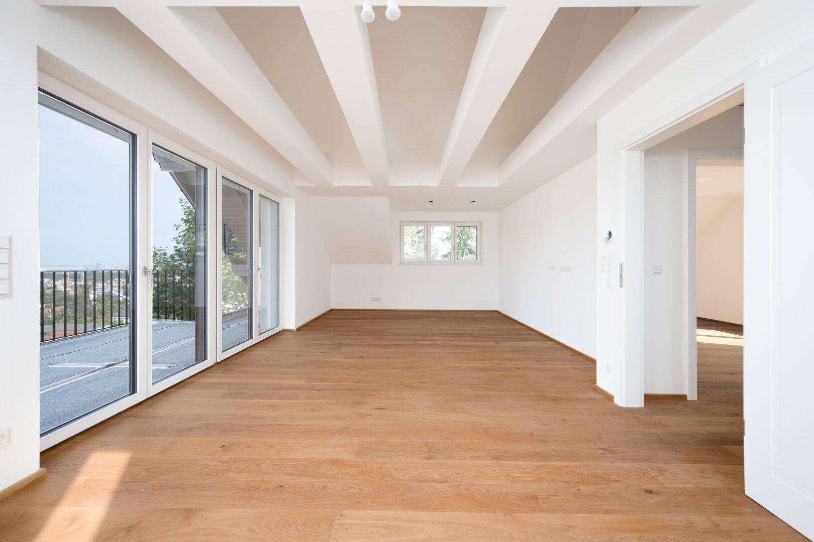 Geräumiger, heller Raum mit Holzboden, hohen Decken und großen Fenstern mit Ausblick.