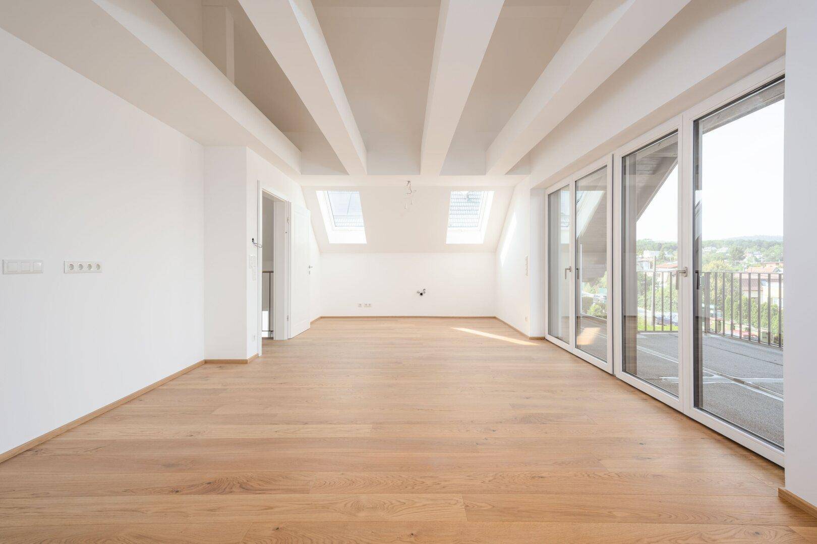 Heller Raum mit Holzboden, Dachfenstern und Zugang zu einer Dachterrasse mit Weitblick.
