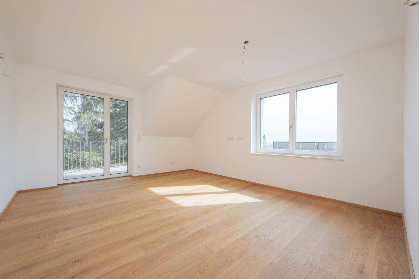 Heller Raum mit Holzboden, Dachschräge und Zugang zu einem Balkon mit Weitblick.