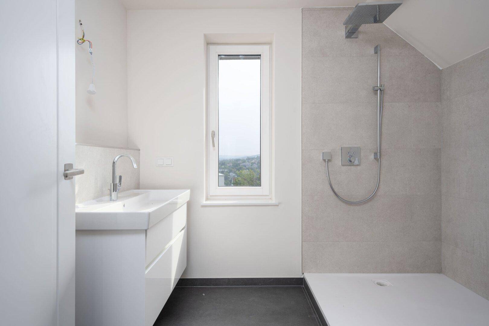 Modernes Badezimmer mit Waschtisch, großer Dusche und Fenster für natürliches Licht.