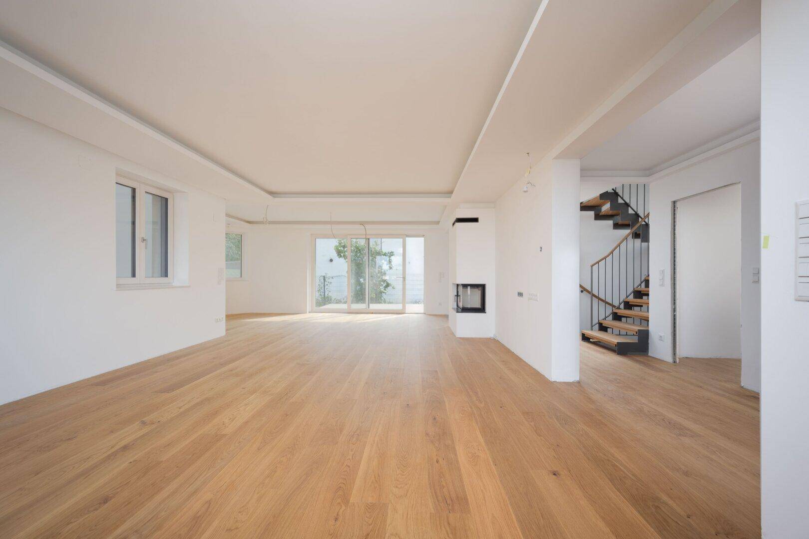 Geräumiger Wohnbereich mit Holzboden, Kamin und offener Treppe, die in die oberen Etagen führt.