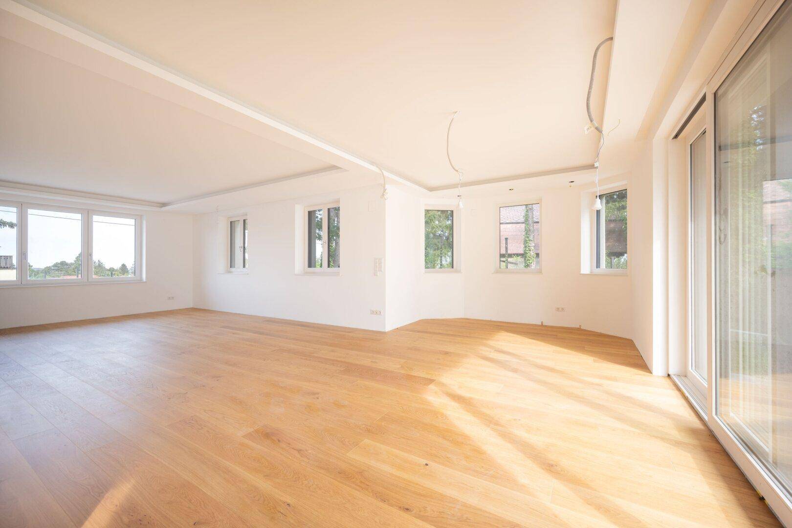 Heller, geräumiger Wohnbereich mit Holzboden und großen Fenstern, die viel Licht hereinlassen.