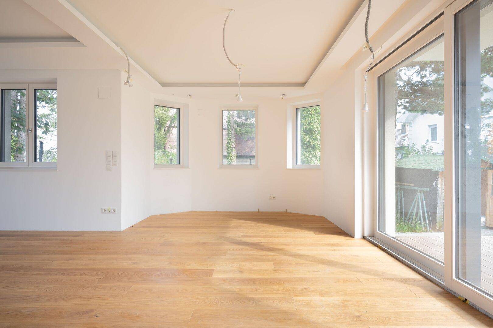 Heller Raum mit Holzboden und vielen Fenstern, die einen Blick ins Grüne ermöglichen.