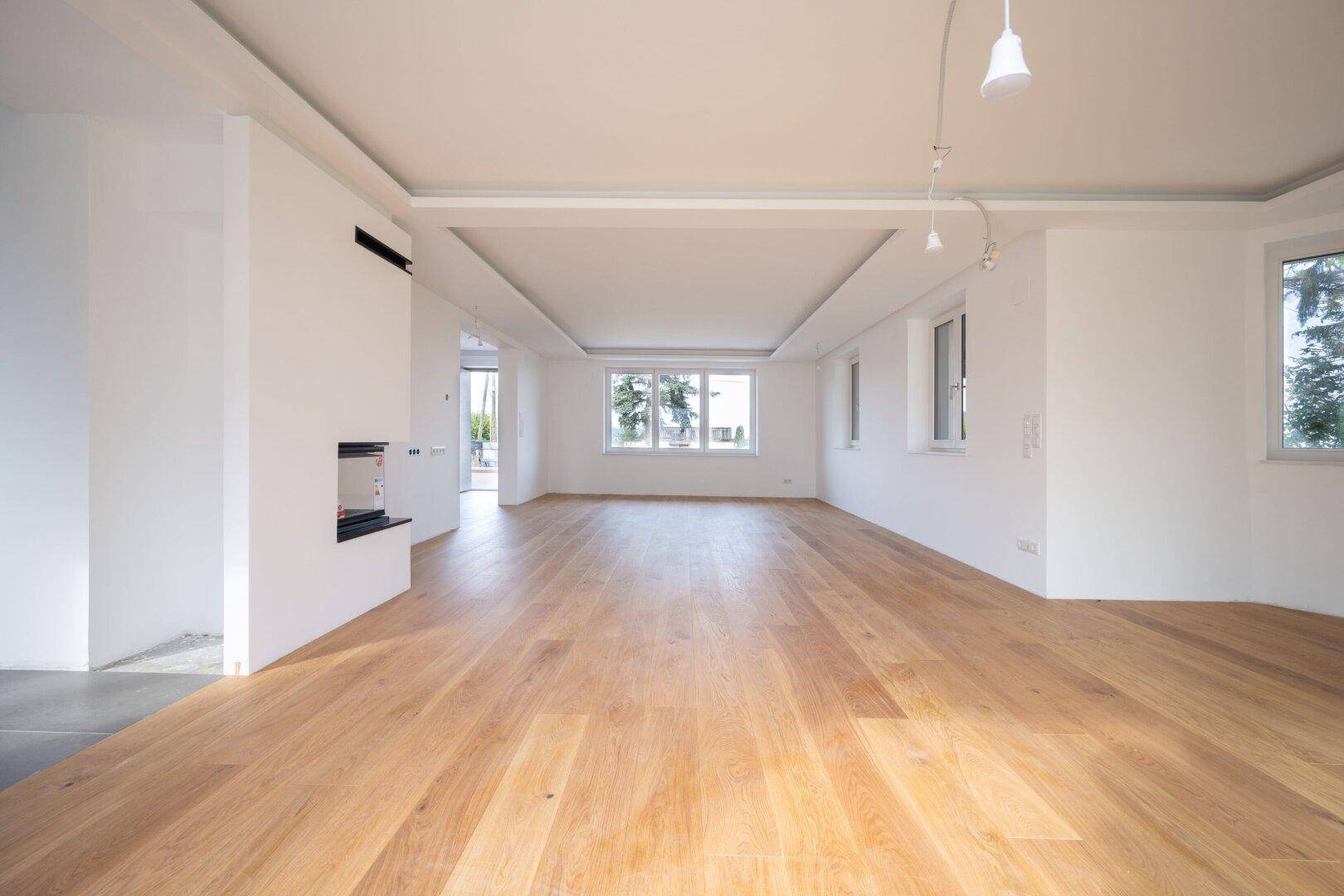 Geräumiger Wohnbereich mit Holzboden, Kamin und großen Fenstern für viel Tageslicht.