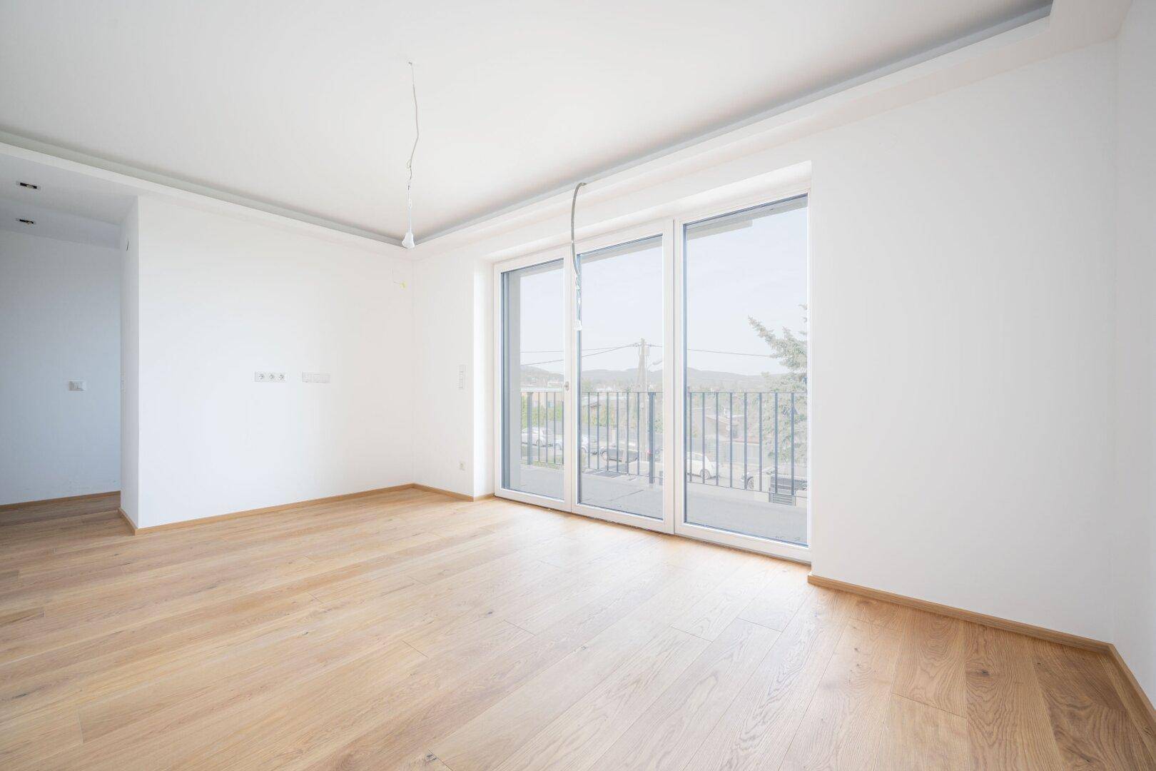 Heller, geräumiger Raum mit Holzboden und großen Fenstern mit Zugang zu einem Balkon.