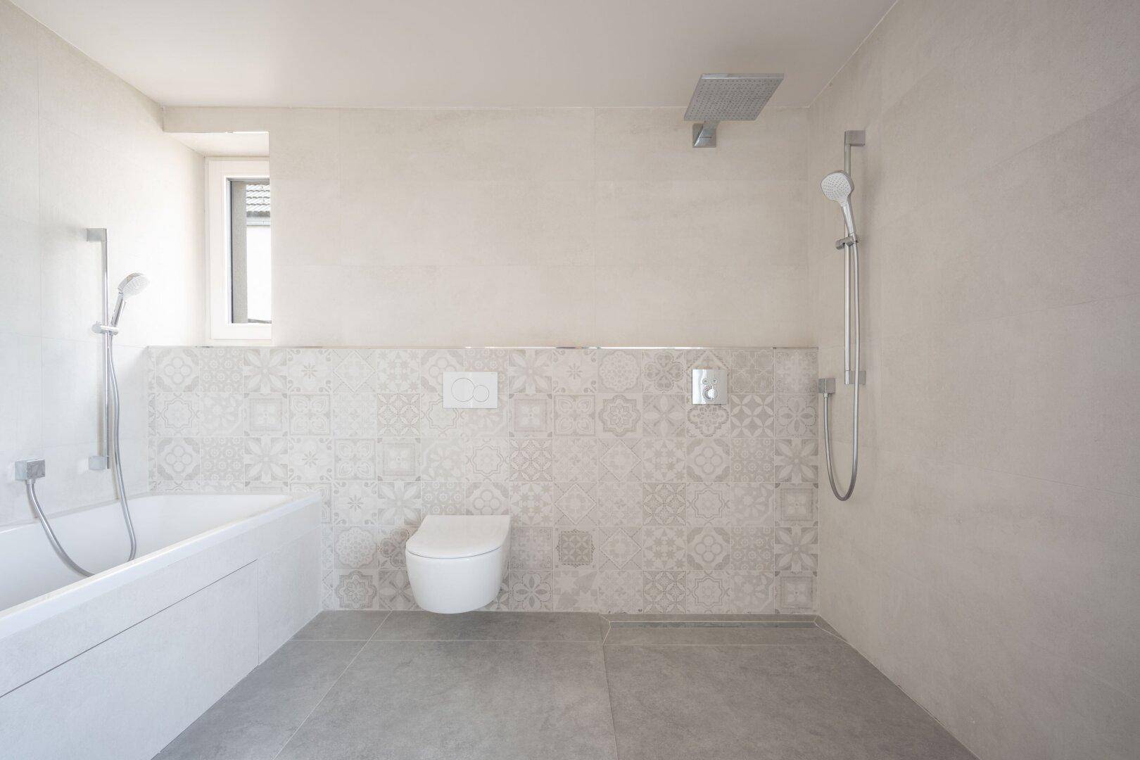 Modernes Badezimmer mit Badewanne, Toilette und Dusche, teilweise mit gemusterten Fliesen.