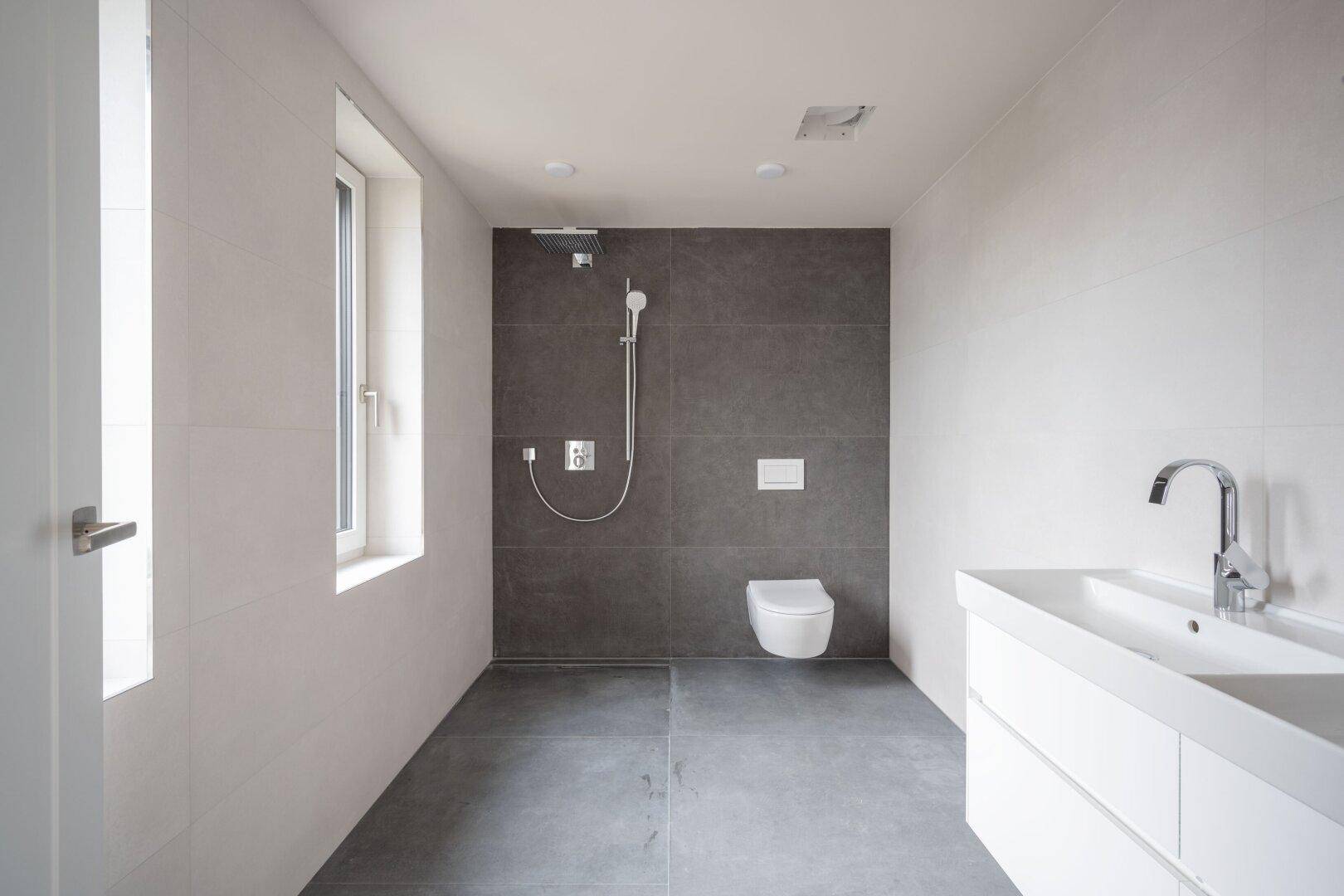 Modernes Badezimmer mit Waschtisch, großer Dusche und Fenster für natürliches Licht.