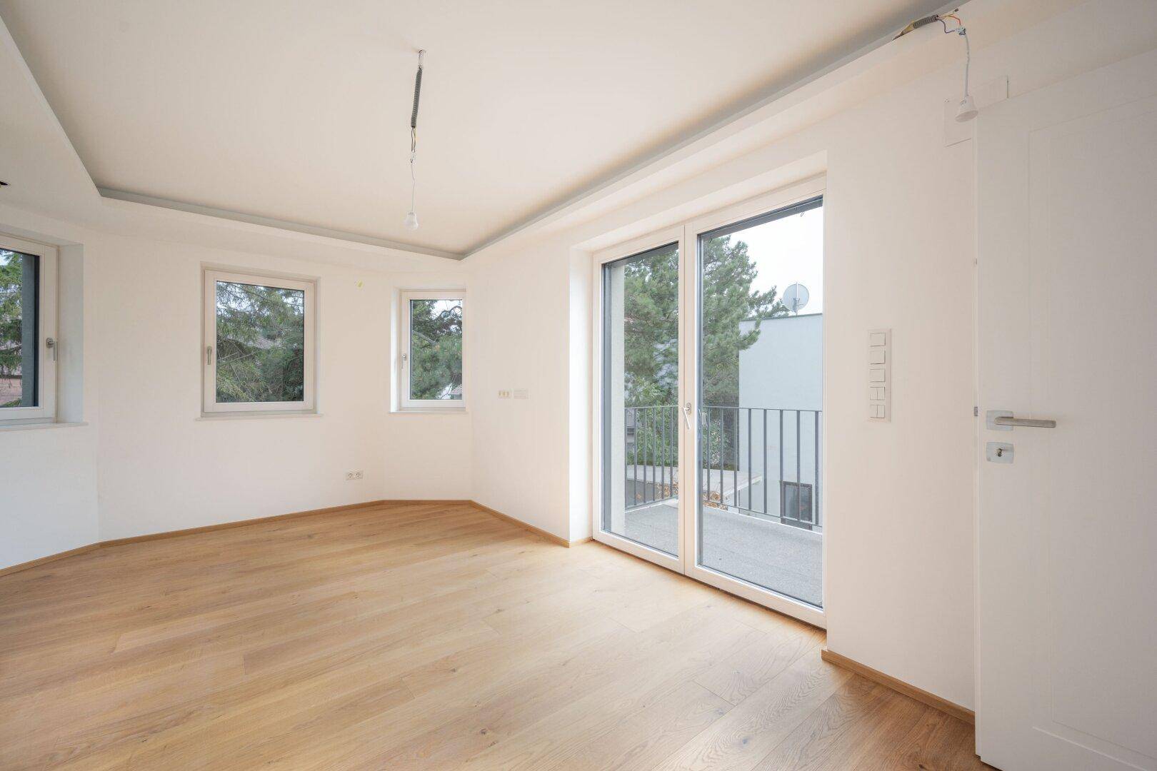 Heller Raum mit Holzboden und Fenstern, inklusive Zugang zu einem Balkon mit Ausblick.