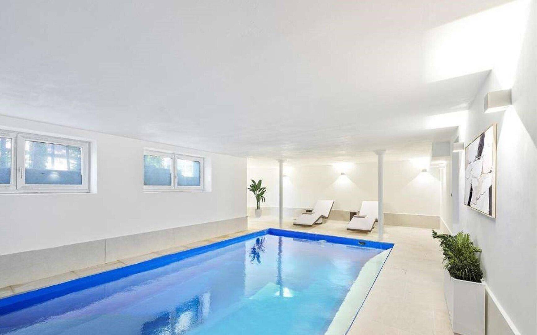 Heller Innenpoolbereich mit Liegestühlen und großen Fenstern für natürliches Licht.