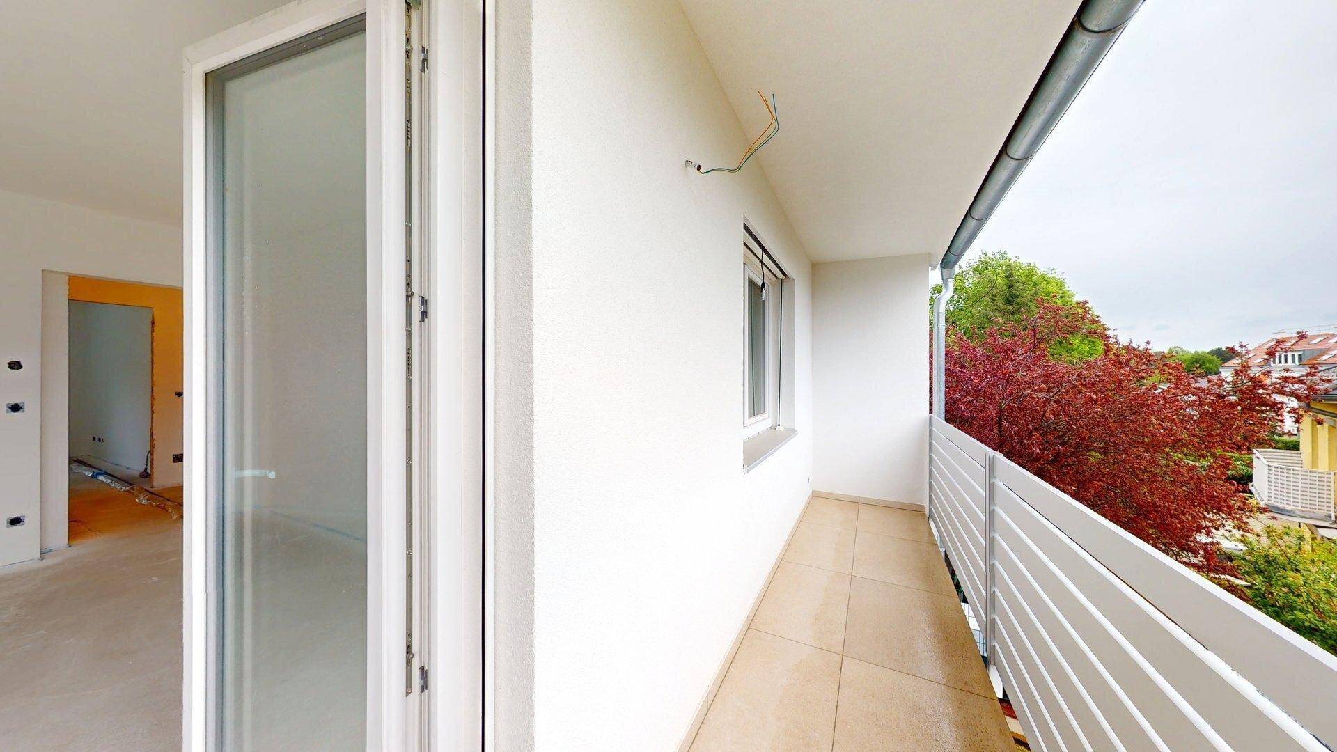 Heller Balkon mit Fliesenboden und weißem Geländer, bietet Blick ins Grüne und auf die Umgebung.