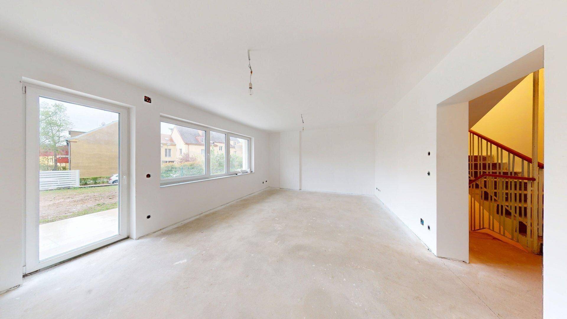 Helles Wohnzimmer im Rohbau mit Zugang zur Terrasse und Blick auf das Treppenhaus.