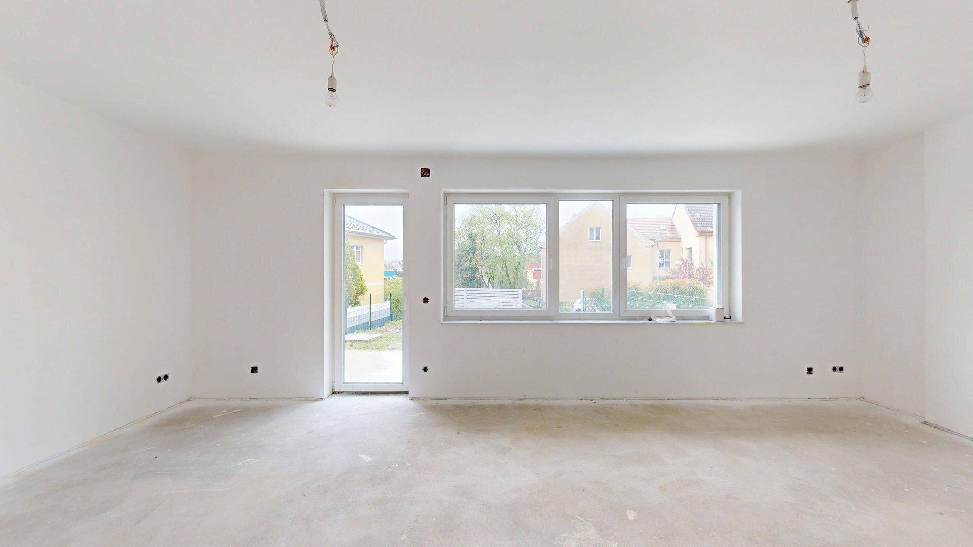 Lichtdurchflutetes Wohnzimmer im Rohbau mit großen Fenstern und Zugang zum Außenbereich.