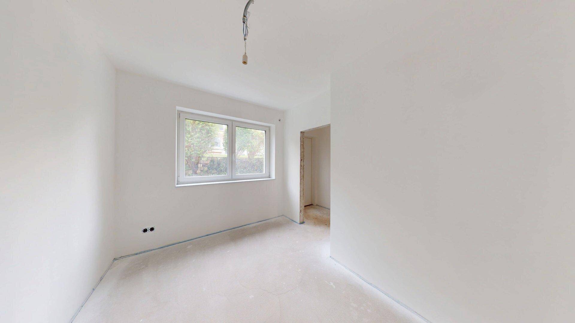 Schlafzimmer im Rohbau mit einem Fenster, das viel Tageslicht in den Raum bringt.