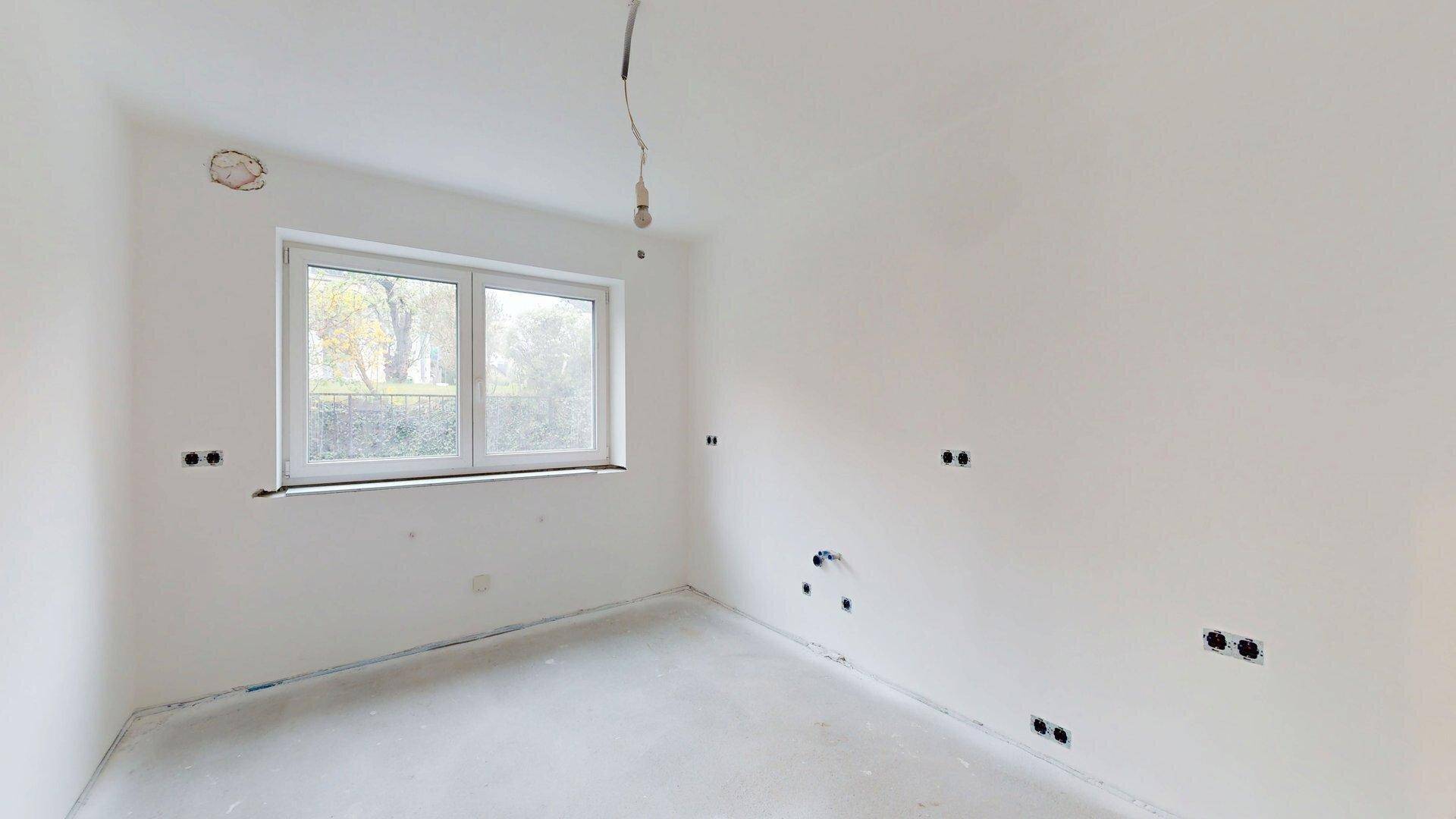 Schlafzimmer im Rohbau mit Fenster und vorbereiteten Elektroinstallationen für den weiteren Ausbau.