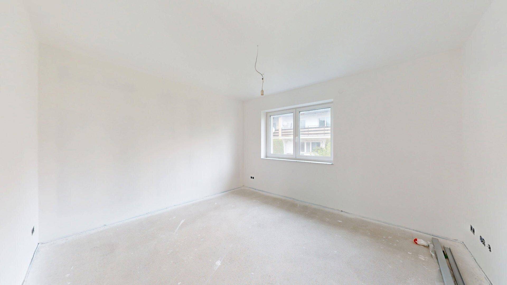 Helles Schlafzimmer im Rohbau mit Fenster und weiß gestrichenen Wänden, bereit für die Endgestaltung.