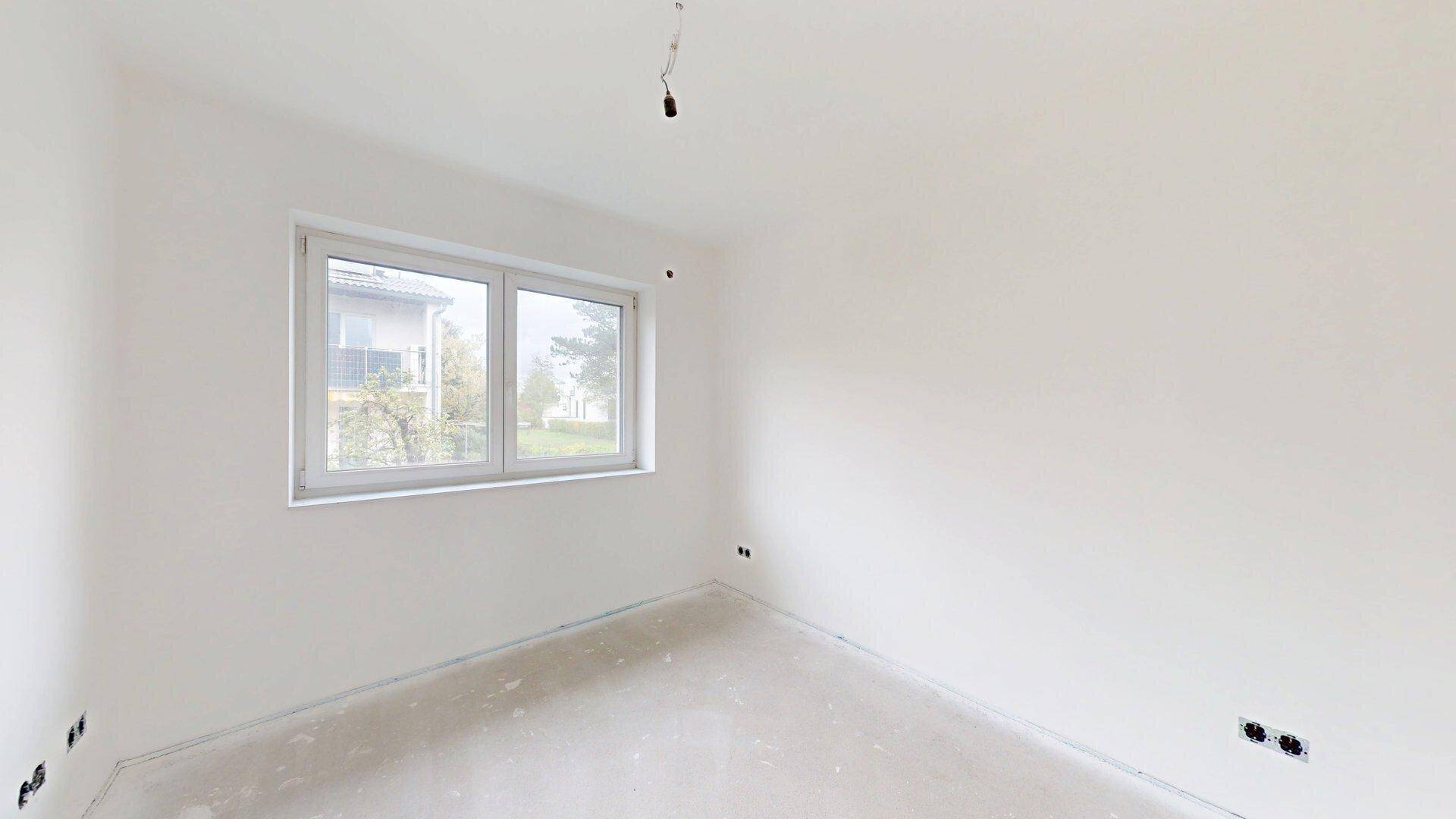 Geräumiges Schlafzimmer im Rohbau mit Fenster, das einen Blick auf die Umgebung bietet.