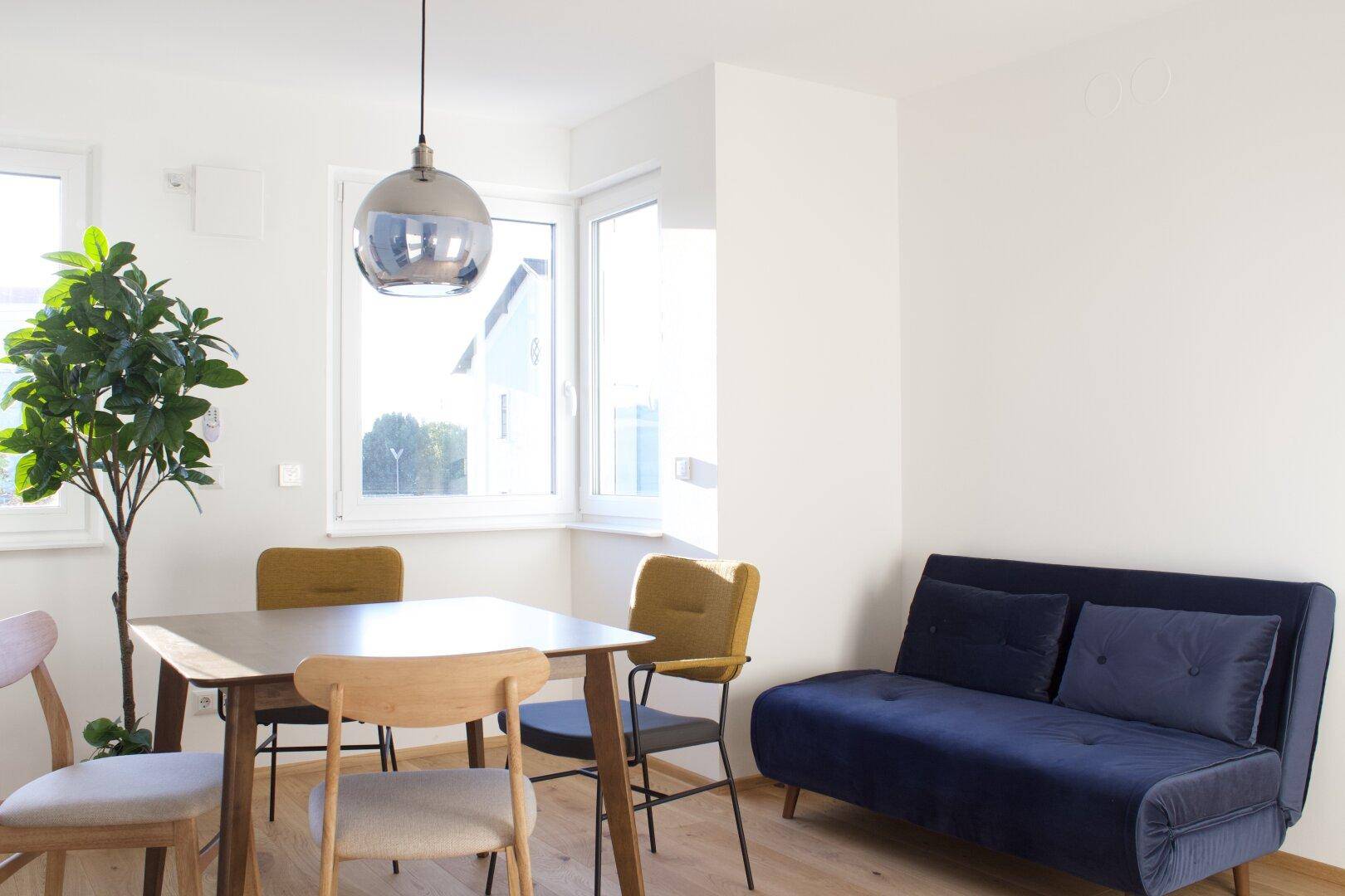 Lichtdurchfluteter Wohn-Essbereich mit gemütlichem Sofa und Blick ins Grüne.