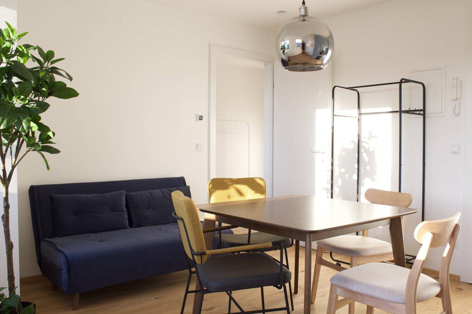 Offener Wohnbereich mit Esstisch, Sofa und Garderobe, hell und modern gestaltet.