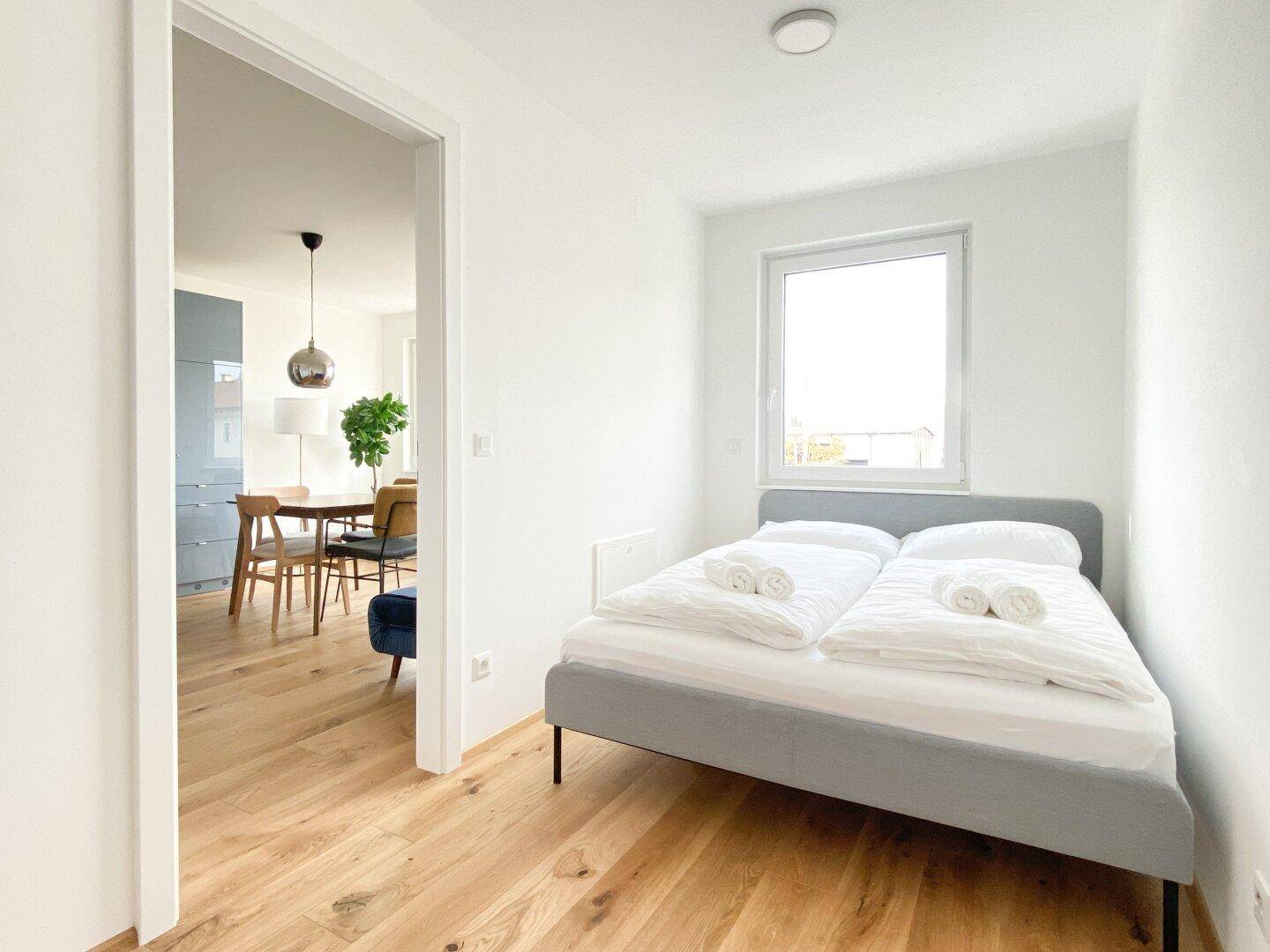 Helles Schlafzimmer mit Holzboden und Blick in den angrenzenden Wohnbereich.