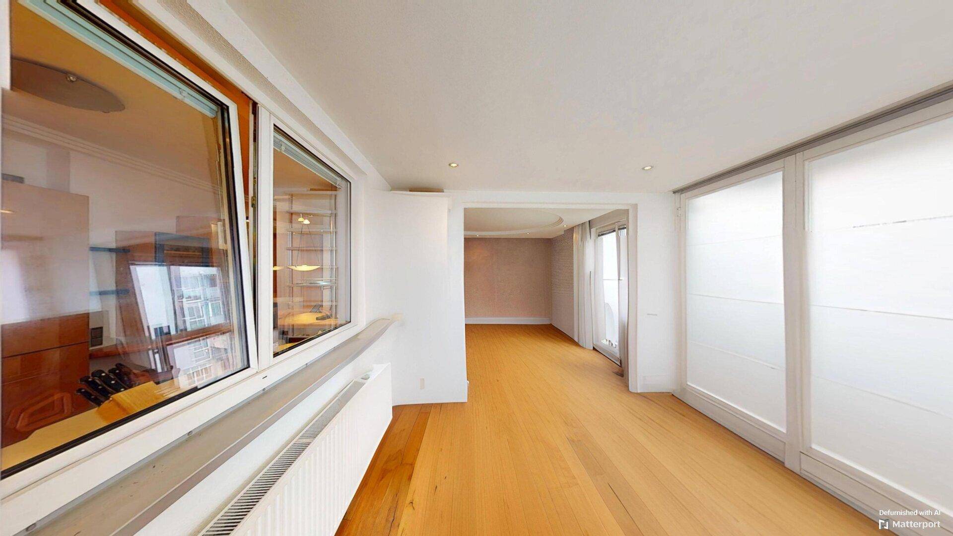 Geräumiges Wohnzimmer mit hellem Parkettboden und Zugang zu einem weiteren Bereich der Wohnung.