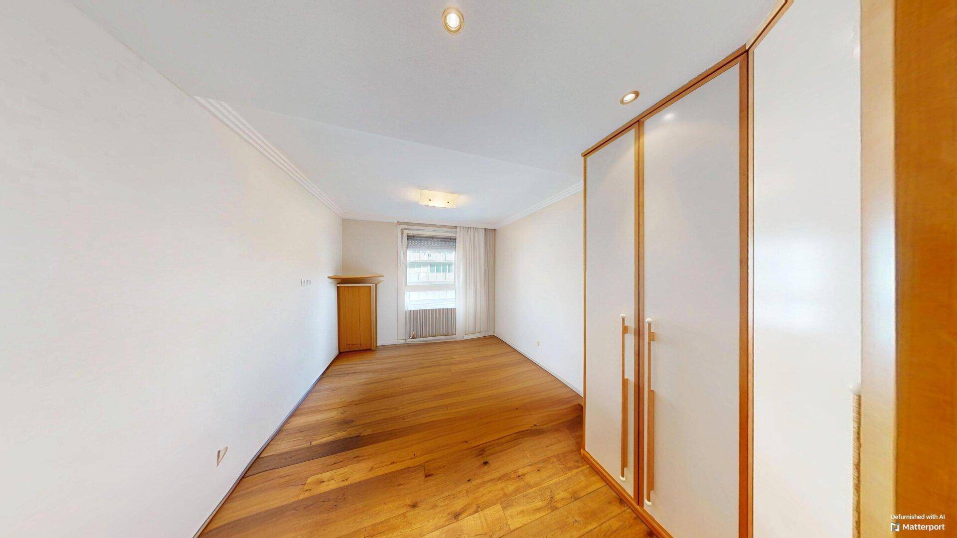 Helles Schlafzimmer mit Parkettboden, weißen Wänden und einem praktischen Einbauschrank.