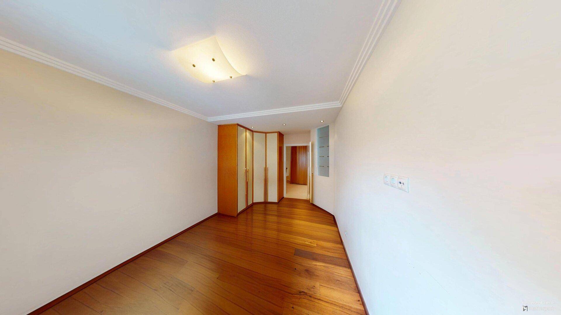 Schlafzimmer mit hellem Parkettboden, weißen Wänden und integrierten Kleiderschränken.