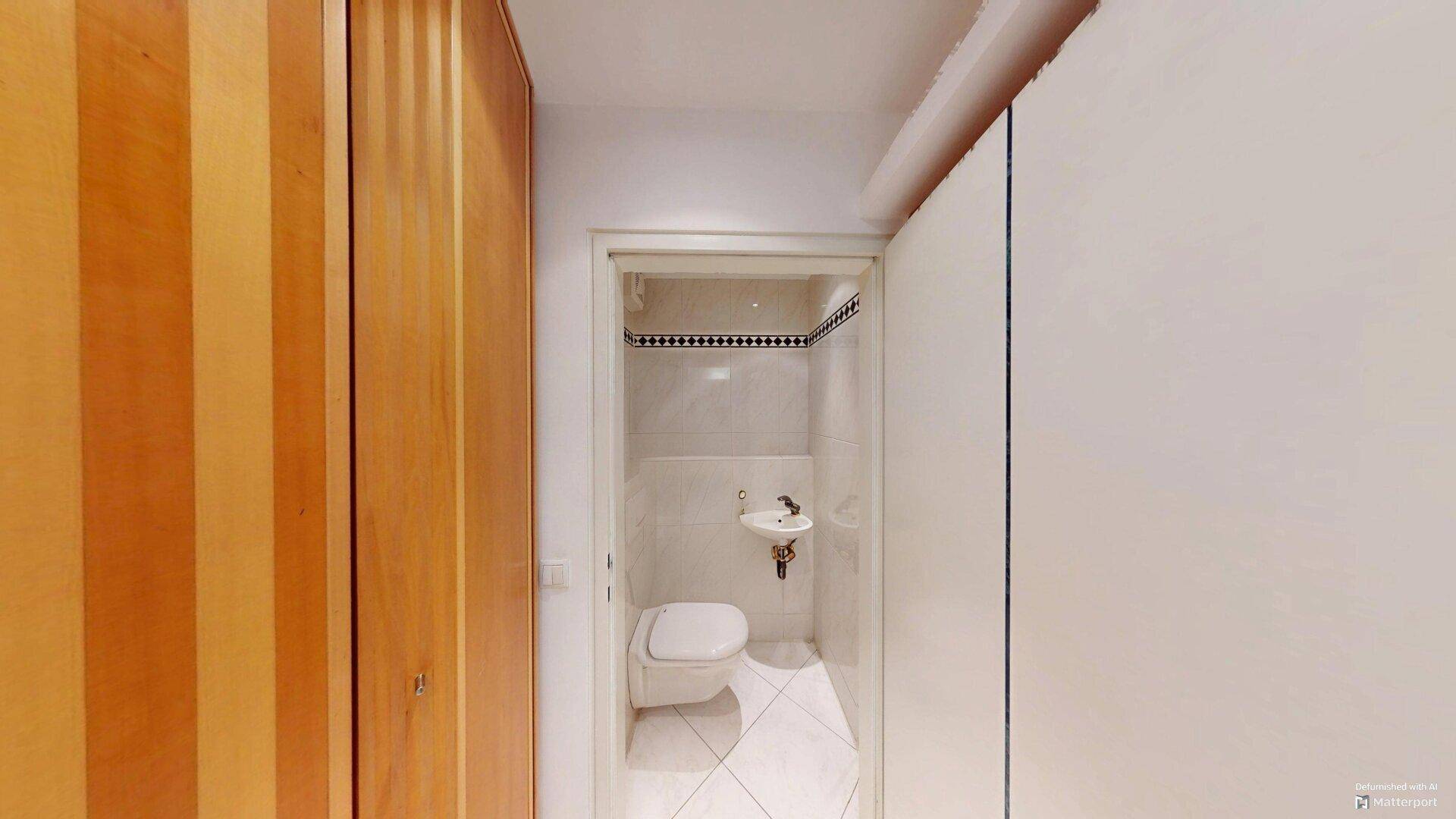 Kleines Gäste-WC mit Toilette, Waschbecken und hellen Fliesen, umgeben von Holzschränken.
