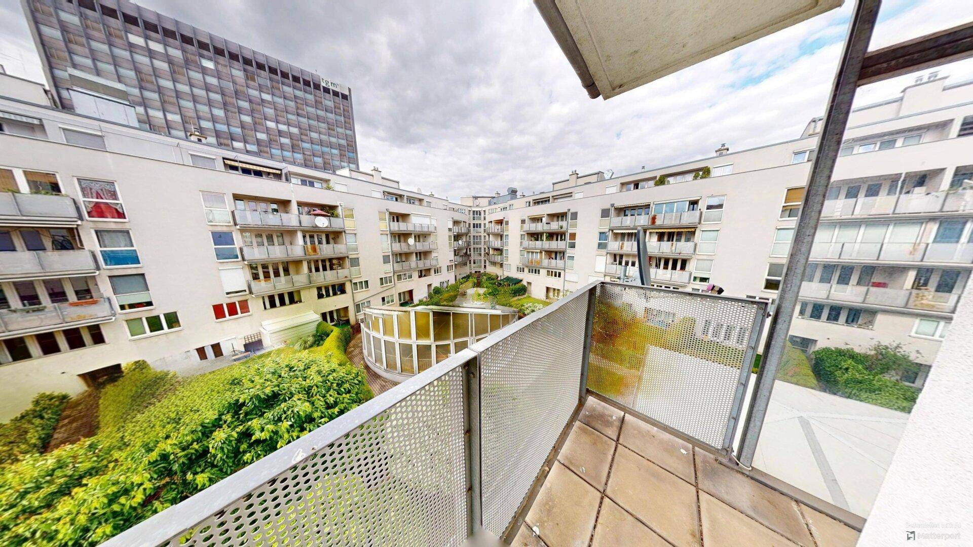 Balkon mit Blick auf einen begrünten Innenhof und die umliegenden Wohngebäude.