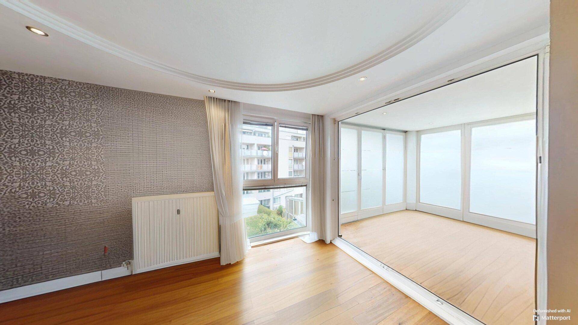 Helles Wohnzimmer mit Parkettboden, einer gemusterten Akzentwand und großen Fenstern mit Ausblick.